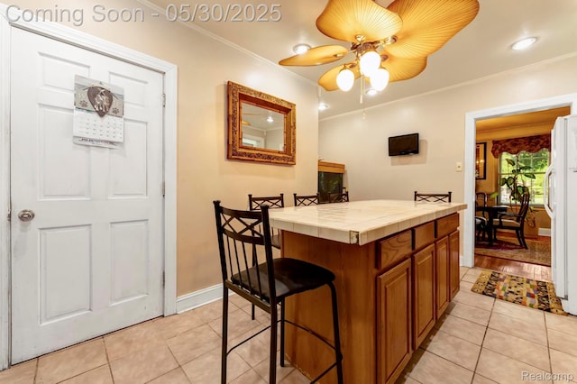 2918 Burns St, Detroit, MI 48214 - kitchen with tile counters, freestanding refrigerator, light tile patterned floors, brown cabinetry, and crown molding
