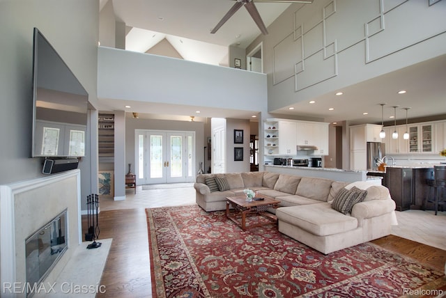 826 Wolverine Dr, Wolverine Lake, MI 48390 - living room with ceiling fan, a fireplace, light wood finished floors, a towering ceiling, and french doors