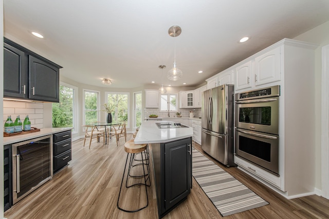 9117 Cambridge Dr, Saline, MI 48176 - kitchen featuring stainless steel appliances, beverage cooler, white cabinetry, decorative backsplash, and light wood finished floors
