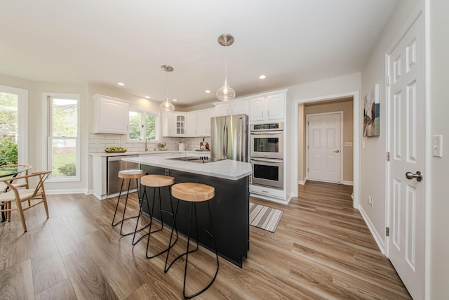 9117 Cambridge Dr, Saline, MI 48176 - kitchen featuring stainless steel appliances, white cabinetry, light wood finished floors, a kitchen breakfast bar, and a center island