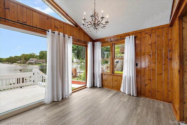 8569 Cooley Beach Dr, White Lake, MI 48386 - unfurnished dining area featuring lofted ceiling, wooden walls, light wood-type flooring, a chandelier, and a water view
