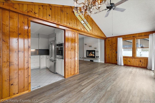 8569 Cooley Beach Dr, White Lake, MI 48386 - unfurnished living room with wood walls, light wood-style floors, a fireplace, a ceiling fan, and a chandelier