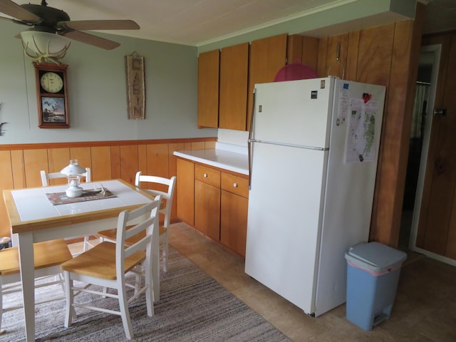 6248 Howard St, Gladwin, MI 48624 - kitchen with freestanding refrigerator, ceiling fan, wainscoting, light countertops, and brown cabinets