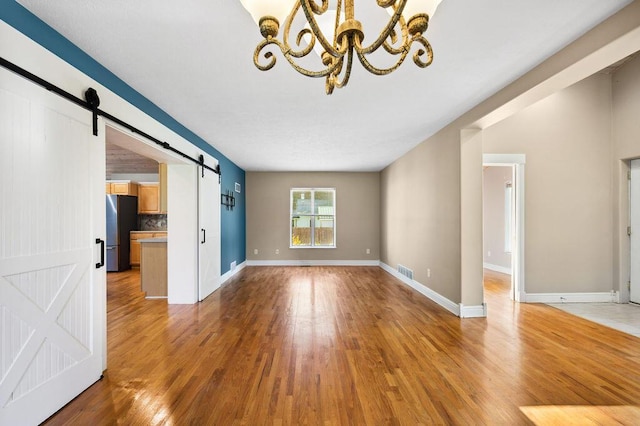 4530 Douglas Ter, Coloma, MI 49038 - unfurnished living room with a barn door, a chandelier, light wood-style flooring, and baseboards