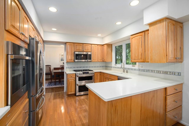 3509 Sulgrave Pl, Ann Arbor, MI 48105 - kitchen featuring stainless steel appliances, a peninsula, a sink, wood finished floors, and tasteful backsplash