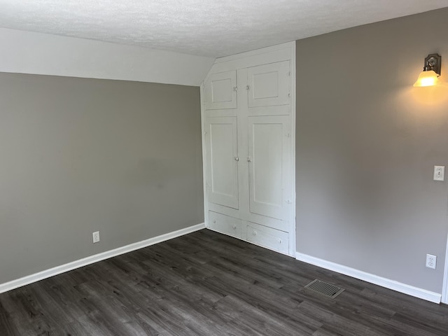 911 Muskegon Ave NW, Grand Rapids, MI 49504 - unfurnished bedroom featuring baseboards, dark wood-type flooring, a textured ceiling, and vaulted ceiling