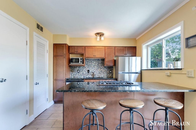 2420 Abbington Dr SE Unit 40, Grand Rapids, MI 49506 - kitchen with stainless steel appliances, brown cabinetry, a sink, tasteful backsplash, and dark stone counters