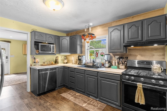 306 Hamilton St, Byron, MI 48418 - kitchen featuring stainless steel appliances, under cabinet range hood, a sink, gray cabinets, and dark wood-style flooring