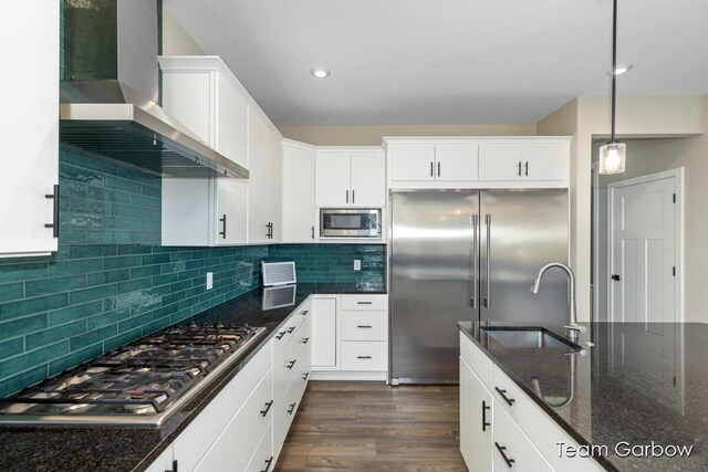 1757 Julienne Ct, Byron Center, MI 49315 - kitchen featuring wall chimney range hood, built in appliances, a sink, dark wood-type flooring, and dark stone counters