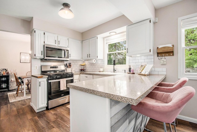 3025 Juneberry Ave SE, Grand Rapids, MI 49508 - kitchen featuring appliances with stainless steel finishes, a sink, a peninsula, white cabinetry, and decorative backsplash