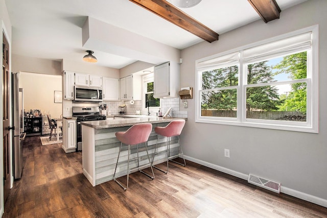 3025 Juneberry Ave SE, Grand Rapids, MI 49508 - kitchen with stainless steel appliances, a peninsula, beamed ceiling, backsplash, and dark wood finished floors
