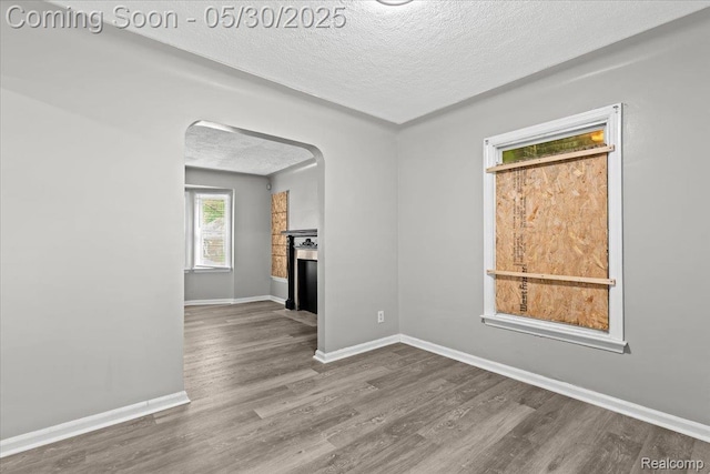 11000 Whitehill St, Grosse Pointe, MI 48224 - unfurnished living room featuring a textured ceiling, wood finished floors, arched walkways, baseboards, and a fireplace