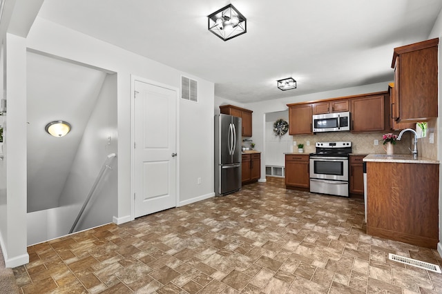 10126 Castle Creek Cir, Galesburg, MI 49053 - kitchen featuring stainless steel appliances, a sink, tasteful backsplash, brown cabinets, and stone finish floors