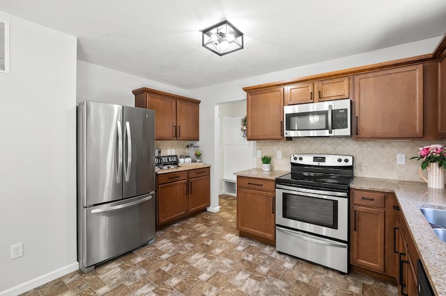 10126 Castle Creek Cir, Galesburg, MI 49053 - kitchen with stainless steel appliances, brown cabinets, decorative backsplash, and light stone countertops