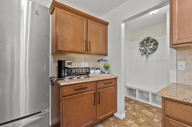 10126 Castle Creek Cir, Galesburg, MI 49053 - kitchen featuring freestanding refrigerator, backsplash, brown cabinets, and light stone counters