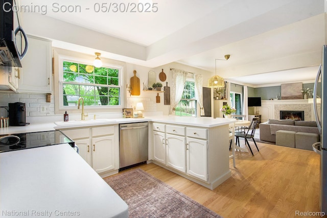 44947 Partridge Dr, Plymouth, MI 48170 - kitchen with appliances with stainless steel finishes, a sink, light wood-style flooring, a large fireplace, and white cabinetry