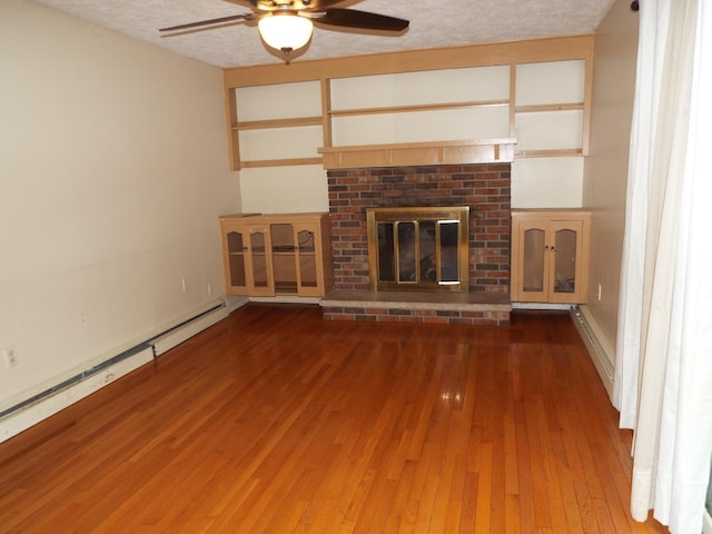 407 Doty St, Leslie, MI 49251 - unfurnished living room with ceiling fan, wood-type flooring, a brick fireplace, a baseboard radiator, and a textured ceiling