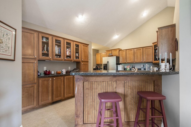 933 Bridge Crest Dr SE, Ada, MI 49301 - kitchen featuring brown cabinets, stainless steel fridge with ice dispenser, vaulted ceiling, a peninsula, and glass insert cabinets