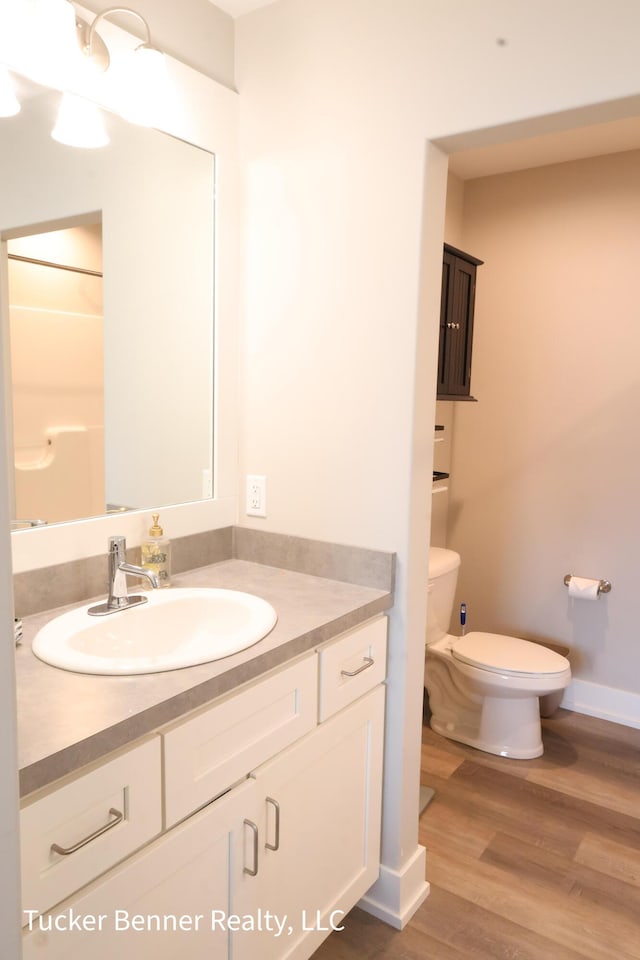 239 Monroe Ave, Muskegon, MI 49441 - full bath with toilet, vanity, wood finished floors, and baseboards