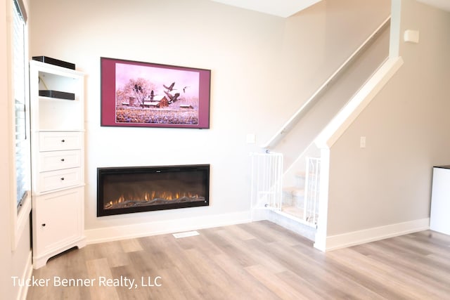 239 Monroe Ave, Muskegon, MI 49441 - unfurnished living room with stairway, a glass covered fireplace, light wood-style floors, and baseboards