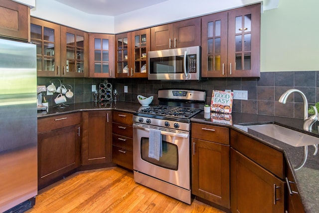 3007 Cedarbrook Rd, Ann Arbor, MI 48105 - kitchen with stainless steel appliances, a sink, light wood-type flooring, dark stone counters, and glass insert cabinets