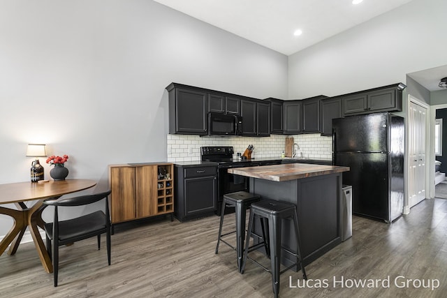 301 NW Xing Unit 25, Holland, MI 49423 - kitchen with black appliances, butcher block countertops, wood finished floors, a towering ceiling, and decorative backsplash