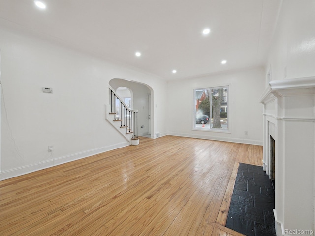 18212 Sorrento St, Detroit, MI 48235 - unfurnished living room with arched walkways, light wood-style floors, a fireplace with flush hearth, stairway, and recessed lighting