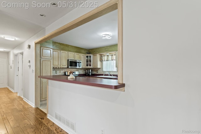 9220 Garden Ter, Commerce Twp, MI 48382 - kitchen with cream cabinets, stainless steel microwave, dark countertops, light wood finished floors, and glass insert cabinets