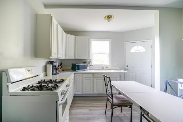 1007 Ionia Ave SW, Grand Rapids, MI 49507 - kitchen featuring white range with gas stovetop, stainless steel microwave, light countertops, light wood-style floors, and white cabinets