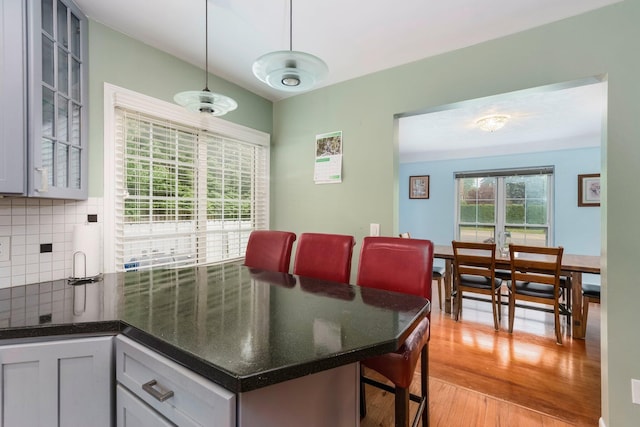 15501 E Jefferson Ave, Grosse Pointe Park, MI 48230 - kitchen with light wood-style floors, decorative backsplash, glass insert cabinets, hanging light fixtures, and dark stone counters