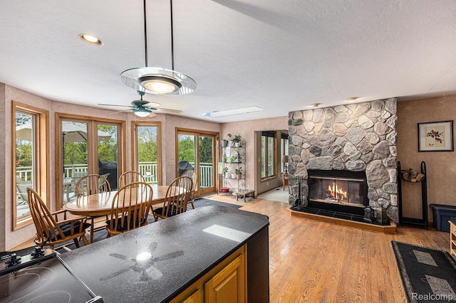 1437 Rillview Ct, Metamora, MI 48455 - kitchen with a textured ceiling, dark countertops, light wood finished floors, a fireplace, and ceiling fan