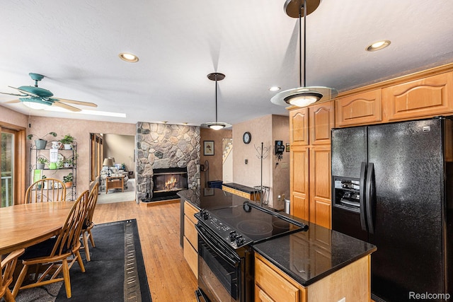 1437 Rillview Ct, Metamora, MI 48455 - kitchen featuring black appliances, a stone fireplace, a ceiling fan, a center island, and light wood-style flooring