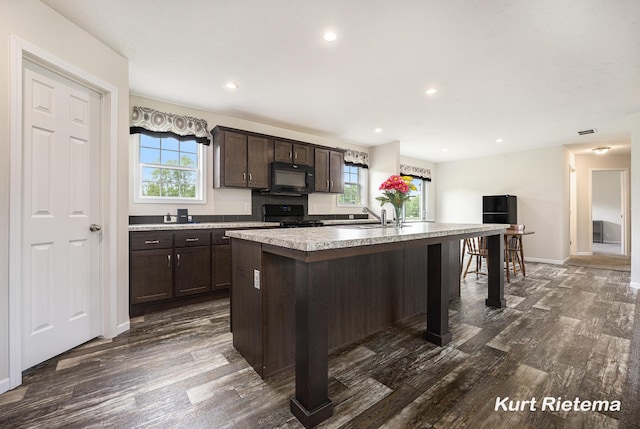 532 48th St, Grand Junction, MI 49056 - kitchen with black appliances, dark wood-style flooring, dark brown cabinetry, a center island with sink, and light countertops