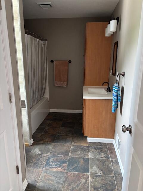 209 S Lake Ave, Fremont, MI 49412 - full bathroom with vanity, baseboards, shower / bath combo with shower curtain, and stone finish floors