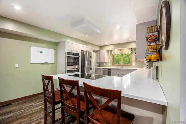 1295 Kern Rd, Oakland, MI 48363 - kitchen with appliances with stainless steel finishes, a peninsula, a breakfast bar area, dark wood finished floors, and light countertops