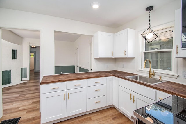 224 Spencer St NE, Grand Rapids, MI 49505 - kitchen with butcher block counters, a sink, light wood-style floors, white cabinets, and pendant lighting