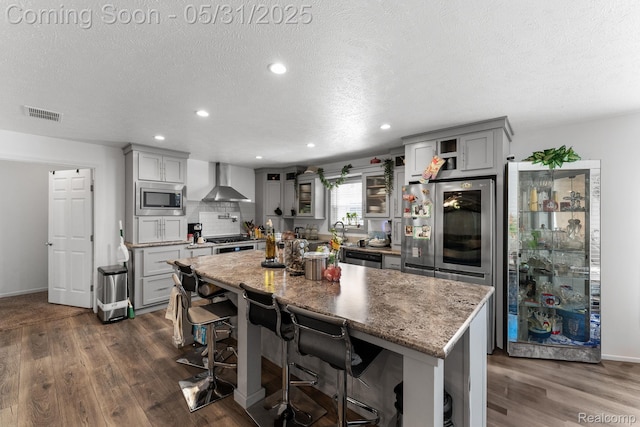 8551 Boyer Dr, Willis, MI 48191 - kitchen with appliances with stainless steel finishes, wall chimney range hood, gray cabinetry, dark wood finished floors, and a breakfast bar