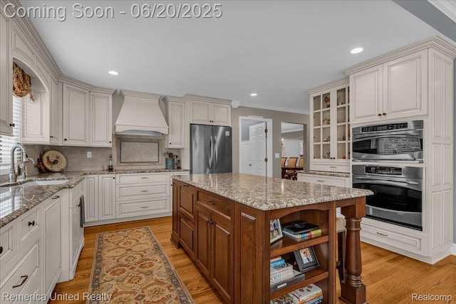 22858 Saint George Cir S, Lyon, MI 48178 - kitchen featuring stainless steel appliances, premium range hood, light wood finished floors, light stone counters, and recessed lighting