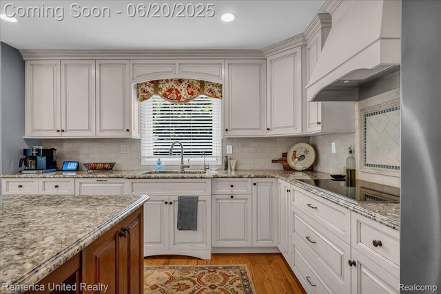 22858 Saint George Cir S, Lyon, MI 48178 - kitchen featuring premium range hood, black electric cooktop, light wood finished floors, decorative backsplash, and light stone countertops