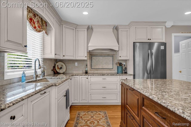 22858 Saint George Cir S, Lyon, MI 48178 - kitchen featuring premium range hood, freestanding refrigerator, light wood-style flooring, backsplash, and light stone countertops