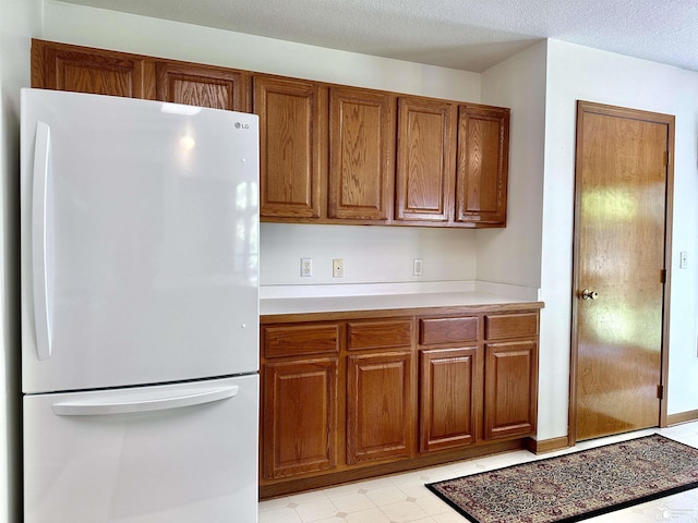 6757 Lockmill Rd, Temperance, MI 48182 - kitchen featuring freestanding refrigerator, brown cabinets, light countertops, and a textured ceiling