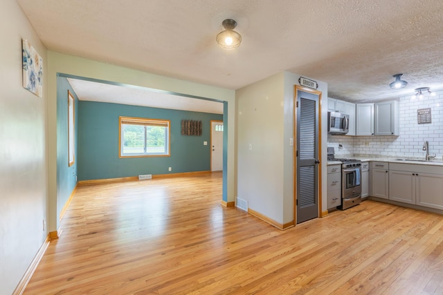 6210 Johnson Rd, Coloma, MI 49038 - kitchen featuring appliances with stainless steel finishes, a sink, light wood finished floors, gray cabinetry, and decorative backsplash