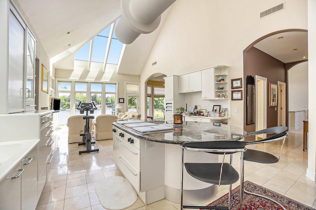 15919 Orchard Point Dr, Spring Lake, MI 49456 - kitchen with a towering ceiling, a kitchen breakfast bar, white cabinetry, arched walkways, and light tile patterned flooring