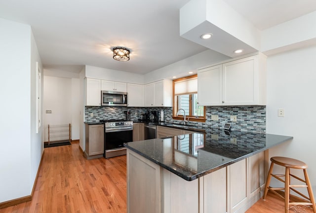 3677 W White Trillium Dr, Saginaw, MI 48603 - kitchen with stainless steel appliances, a sink, a peninsula, dark stone countertops, and light wood finished floors