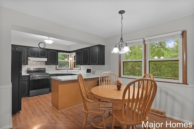1724 Sandra St NW, Grand Rapids, MI 49544 - kitchen featuring gas stove, under cabinet range hood, dark cabinetry, freestanding refrigerator, and a peninsula
