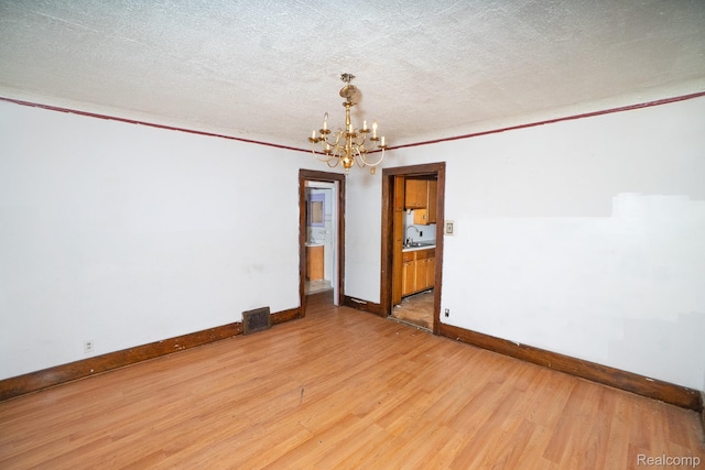 12151 Corbett St, Detroit, MI 48213 - unfurnished room with a chandelier, baseboards, light wood finished floors, a sink, and a textured ceiling