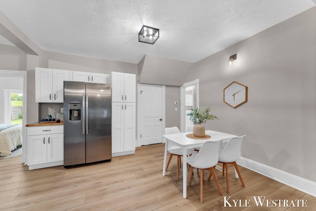 810 James St, Belding, MI 48809 - kitchen with stainless steel fridge with ice dispenser, a textured ceiling, light wood-style floors, white cabinetry, and vaulted ceiling