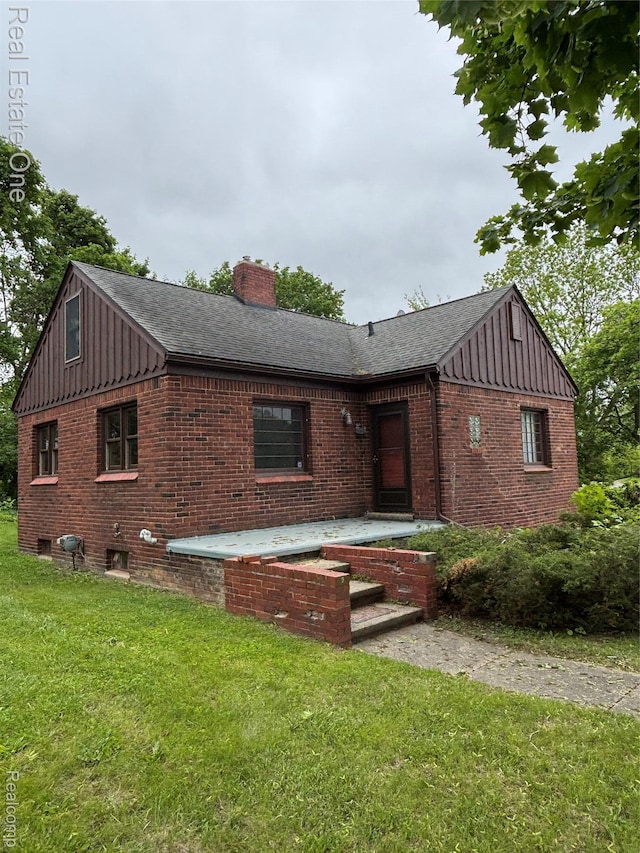 109 W Kennett Rd, Pontiac, MI 48340 - view of front facade with board and batten siding, brick siding, a front yard, a chimney, and roof with shingles