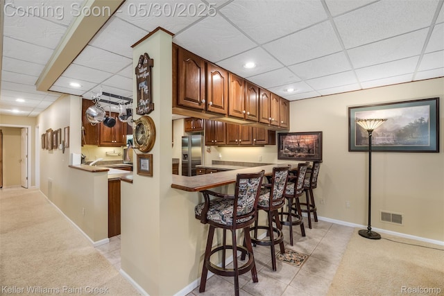 3120 Pond Rd, Leonard, MI 48367 - kitchen with stainless steel fridge, a paneled ceiling, a breakfast bar area, recessed lighting, and light colored carpet