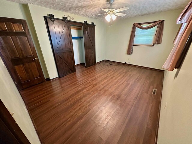 19379 Lincoln Rd, New Lothrop, MI 48460 - unfurnished bedroom with dark wood-type flooring, a textured ceiling, a barn door, baseboards, and a ceiling fan